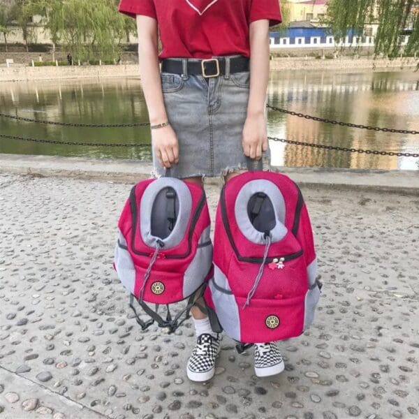 Person holding two pink pet carrier backpacks.