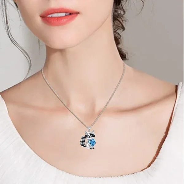 Silver necklace with raccoon charm and blue stone.