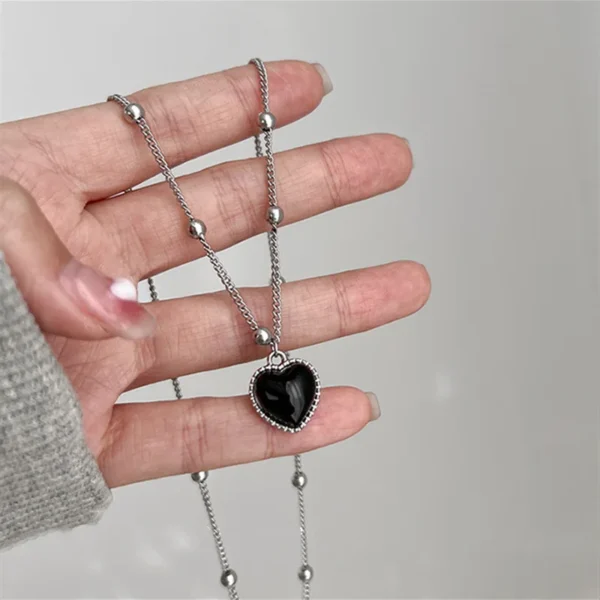 Silver chain necklace with black heart pendant.