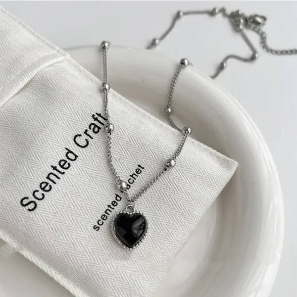 Silver chain necklace with black heart pendant.